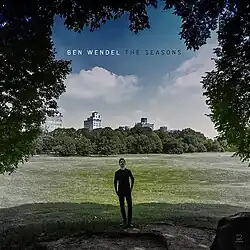 Square photo with Ben Wendel center in a park field with a blue sky and cumulus clouds above