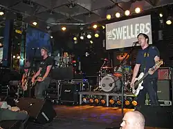 Four men performing onstage playing and singing into microphones