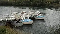 A dock spanning to a punt ferry in a river, a platform at the end of the dock resting on two small boats