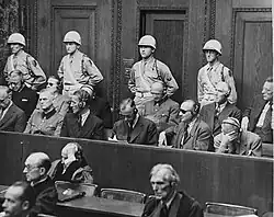 Seated men wearing headphones, with soldiers standing behind them