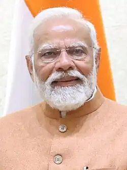 A cropped color photograph, from the chest up, of a bespectacled, bearded aged man