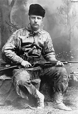 Black and white photo of a middle-aged man in hunting attire with a rifle