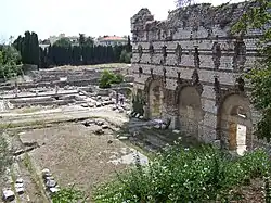 Ruins. On the right a stone wall with brick bonding, pierced by two vaulted entrances