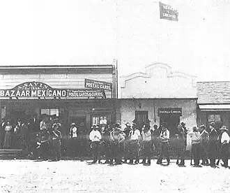 Men holding rifles, standing in front of a Mexican bazaar