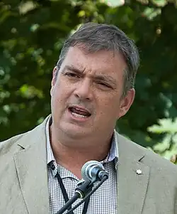 Tim Cook at the Eden Mills Writers' Festival in 2017, medium shot of a caucasion male in their 40s, with greying hair, and Shure Brothers SM58 microphone in front of him.