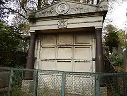 Tomb of General d'Aboville, with some damage from time, it is fenced off with some overgrowth of vegetation. The columns that support the structure at the front are engraved with battles fought by members of the Aboville family.