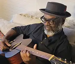 Sims playing acoustic guitar, 2024