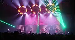 Musicians performing on stage in front of a crowd under many lights of different colors.