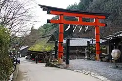Large red torii next to a wooden thatched house.