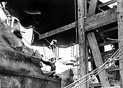 The explosive force tore and dished in the steel side plating. A wooden scaffold has been erected to the right for repair work.