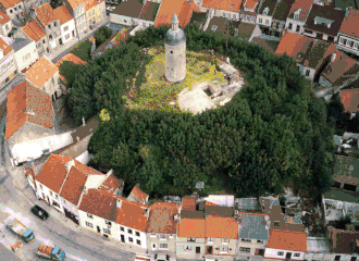 An aerial colour photograph of stone-built tower on a grassy and wooded mound, surrounded by houses