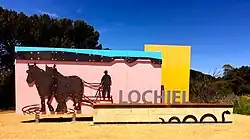 The town entrance sign at Lochiel, depicting the seasonal pink colouration of Lake Bumbunga, the nearby hills, and horses pulling a salt scrape; the low wall in front depicts the "Loch Eel"