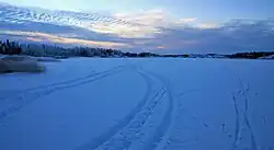 The lake covered with snow, in which tracks of tires and skis are visible