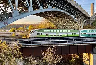 A green-and-white GO train passing under the large arch bridge of York Boulevard in Hamilton, Ontario.