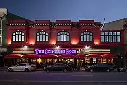 Front view of The Stinking Rose restaurant in San Francisco at dusk, showing its red building exterior with arched windows, neon signage, and red awnings over the sidewalk dining area.