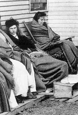 Women sitting in a row, covered in blankets. Mallon is looking straight at the camera
