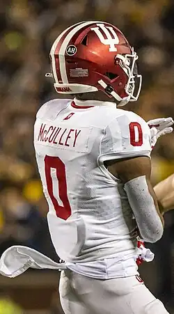 Indiana Hoosiers quarterback Donaven McCulley is wearing an Indiana Hoosiers jersey with the picture showing the backside of it, with "McCulley" written at the top in smaller text and the bigger number 0 shown beneath his name. The jersey color is white with the text and number being red. McCulley is also wearing a red helmet with a white Hoosier logo and three stripes also on it.