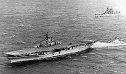 A black and white photo of an aircraft carrier and a battleship in the background