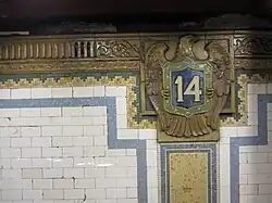 A beige, green, and blue cartouche on the wall of the station with the number "14" in white text