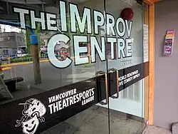 A close-up of glass double-doors with white text decals on them that says "The Improv Centre - Licensed - Vancouver TheatreSports League - World Renowned Live Comedy Improv"