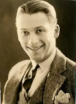 Sepia studio portrait of a smiling young man with slicked-back hair wearing a suit and tie