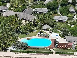 Aerial photo showing a thatched-roof beach lodge surrounded by palm trees along a sandy coastline in Vilankulo, Mozambique.