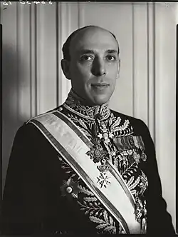 Upper-body portrait of middle-aged, balding man standing, frowning, in formal ambassadorial clothing