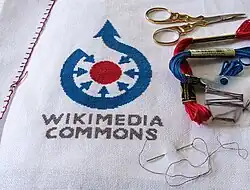 A cross stitch approximation of the Wikimedia Commons symbol using three thread colors and 28 count Aida cloth. The image is a focus stack of 9 images.