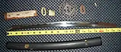 An antique Japanese wakizashi with koshirae and related parts, shown disassembled. The hamon (temper line) is clearly visible.