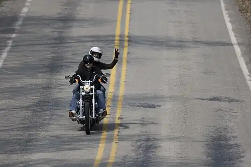 A motorcycle passenger using a V sign