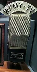 An old microphone with a custom W F M Y - TV label on the top