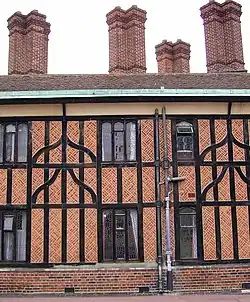 A close-up of a building made with black timbers and red brick. The building has four tall, brick chimneys. A relatively modern drainpipe comes down the middle of the building.