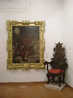 A full-body portrait of the king in an elaborate frame is displayed next to an antique chair.