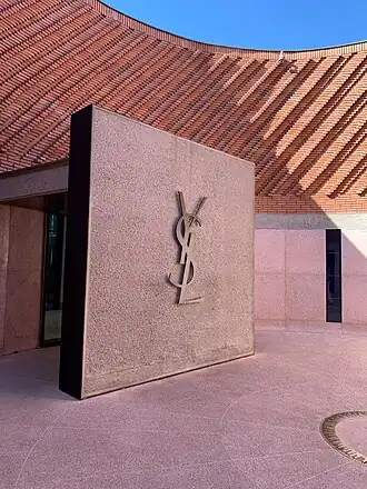 Pink stone walls and a curved brick facade in a modern courtyard with a large metallic Yves Saint Laurent logo mounted on a square wall.