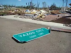 The Yazoo City sign knocked over on a road with ruins in the background