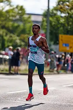 A man wearing a white top and tight grey shorts running as if he is floating above the street