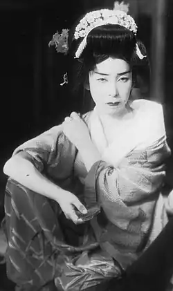 A Japanese woman wearing an ornate headpiece and and kimono, staring at the camera with a somber expression
