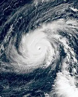 A satellite photograph of Typhoon Yutu as an extremely powerful tropical cyclone over the Western Pacific. The cyclone features intense, thick convection surrounding a well-defined eye and two rainbands wrapping into the center from the north and south. Cirrus clouds sprout from these bands, indicating that the storm has good outflow.