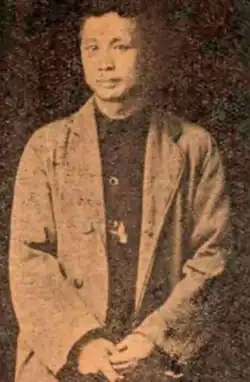 Black-and-white sepia-toned picture of Zhang Jingsheng, wearing a jacket and holding his hands together in front of himself