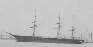 Black and white photo of a three-masted ship with a complete gundeck moored in a harbor.