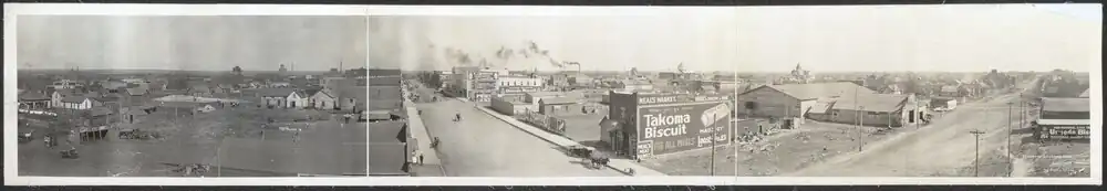 A panoramic view showing wooden houses and businesses, many along two main dirt roads that meet at a corner