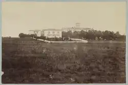black and white photo of field with several buildings in the distance
