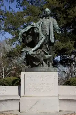 A color photograph of a monument consisting of a stone base and metal statue