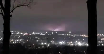 A partly-visible tornado illuminated by a bright flash between two trees