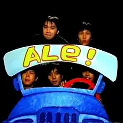 It illustrates the specific creative direction (the "ALE!" prop/blue car featuring five band members) discussed in the article, which cannot be captured by text alone.