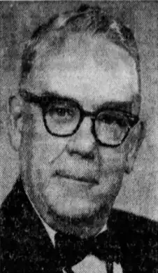 Black and white photo of a late middle-aged man wearing dark-rimmed eyeglasses, black suitcoat, white dress shirt, and a black bow tie