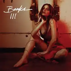 An album cover featuring Banks seated on the floor in front of a wall, with bent legs and one hand positioned near the neck