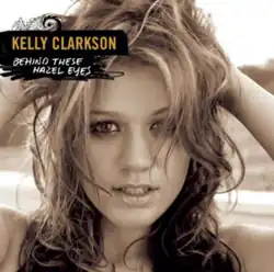A black and white frontal image of Clarkson holding her curly hair at the back of her head: She is looking in front. On her upper left, the word "Kelly Clarkson" and "Behind These Hazel Eyes" are written in yellow and white capital letters respectively.