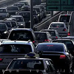 Cars lined up on a freeway with the artists name written along the bottom