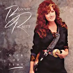 photo of Bonnie Raitt in black with leopard top, large belt buckle and guitar slung low